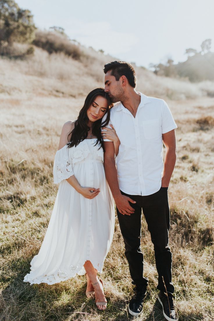 a pregnant woman standing next to a man in a field