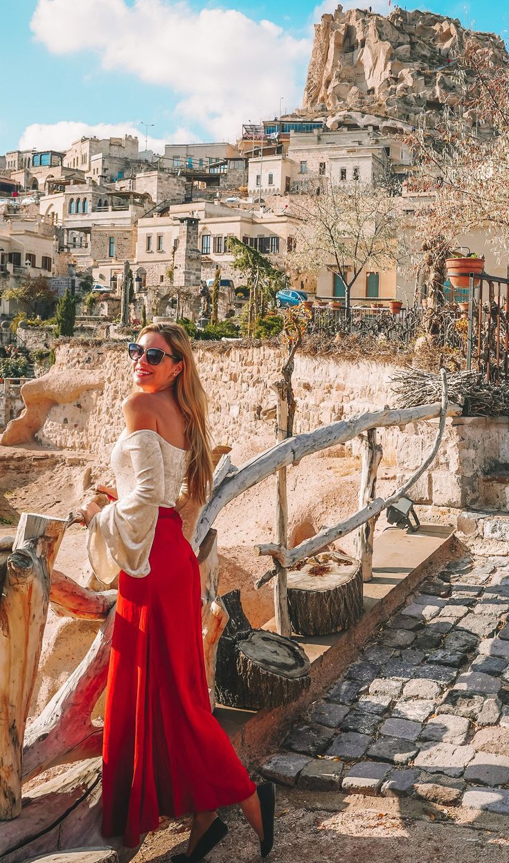 a woman in a red dress is standing on a stone walkway and looking off into the distance