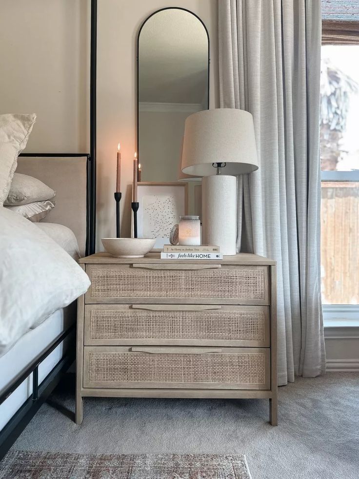 a white bed sitting next to a window with a lamp on top of the dresser