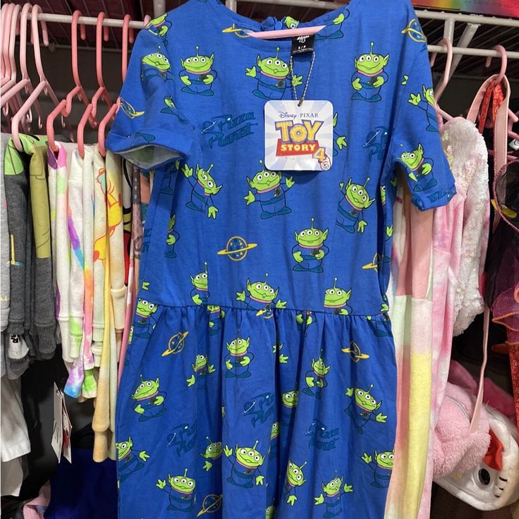 there is a blue dress with green aliens on it in front of other clothing racks