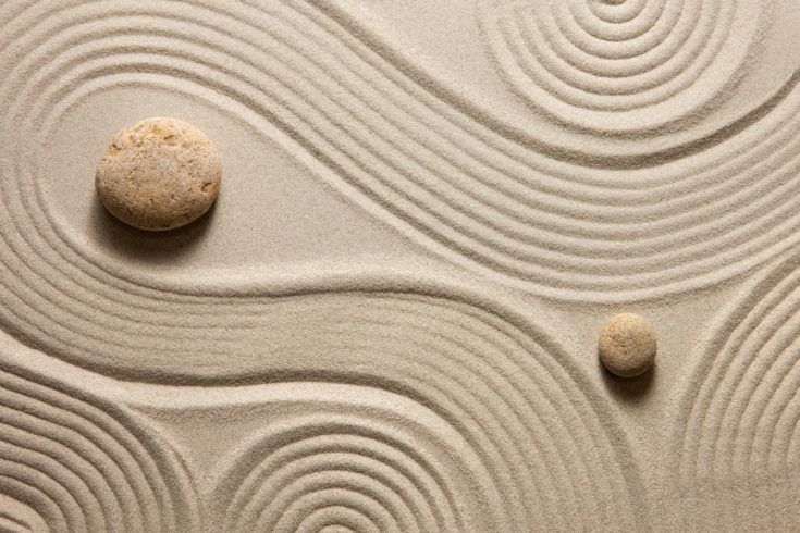 two rocks sitting on top of sand with swirls and waves in the background stock photo