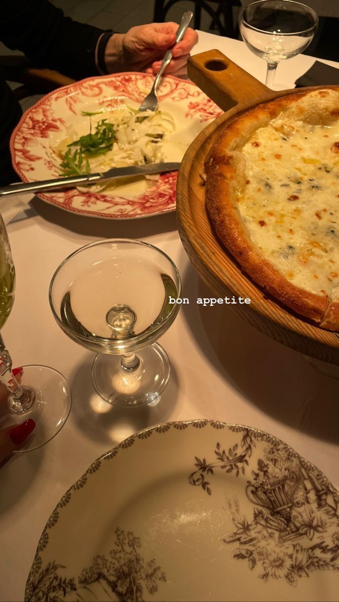 a table topped with plates and bowls filled with food next to wine glasses, cheese pizza