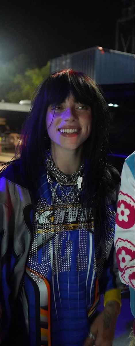 a woman standing in front of a building at night with her eyes closed and smiling