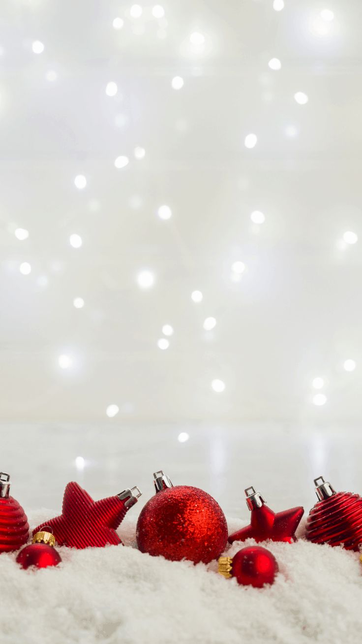 red christmas ornaments on white fur with lights in the backgroung behind them