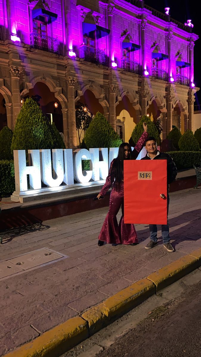 two people standing on the side of a road with a sign in front of them