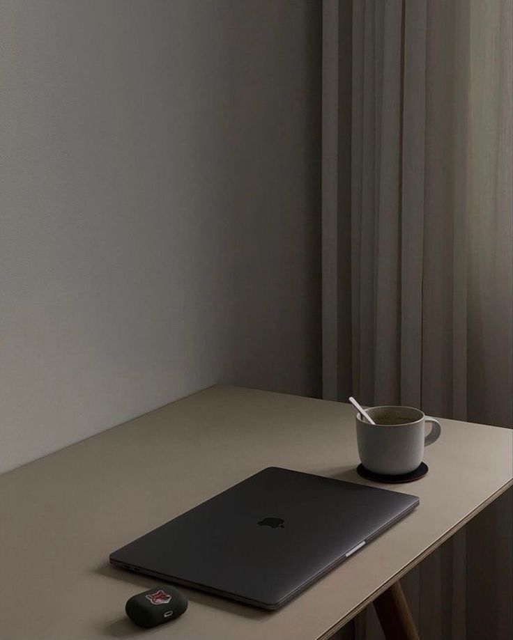 a table with a laptop, mouse and coffee cup on it next to a window