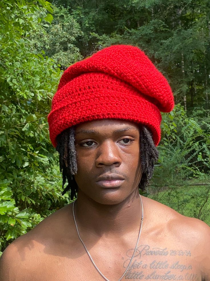 a man wearing a red knitted hat with tattoos on his arm and chest is looking at the camera