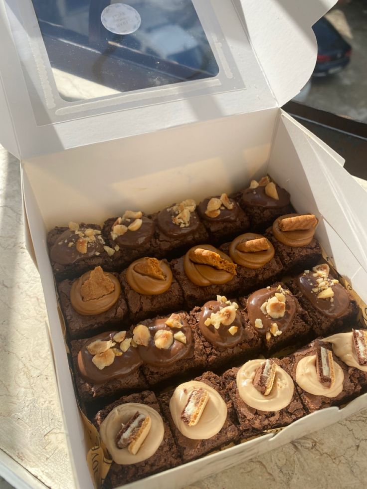 a box filled with lots of brownies covered in frosting and nuts on top of a counter