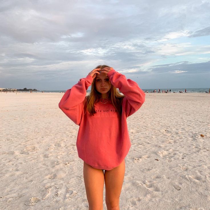 a woman standing in the sand with her hands on her head and looking at the camera