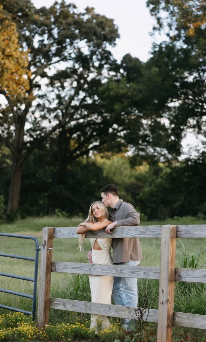 a man and woman standing in front of a fence with their arms around each other