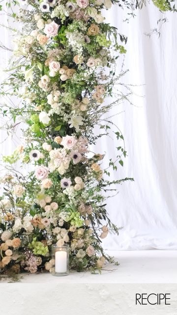 an arrangement of flowers and greenery is displayed on a white surface with a candle