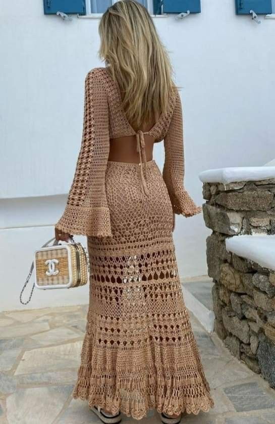 a woman in a crochet dress is standing on a stone walkway with her back to the camera