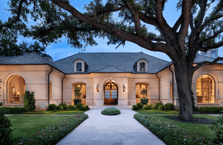 a large house with lots of windows and trees in the front yard at night time