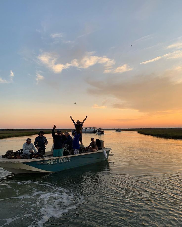 a group of people riding on top of a boat in the water at sunset with their arms up