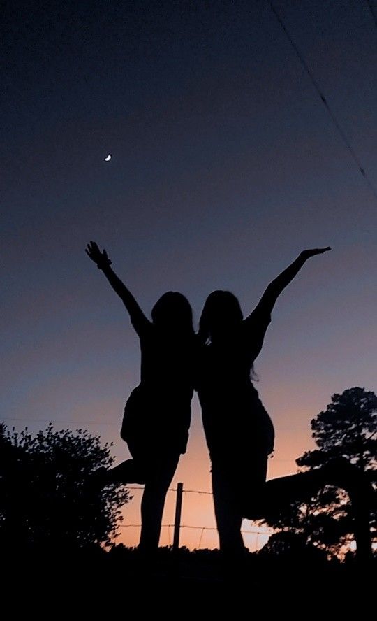 two women standing in the dark with their arms outstretched