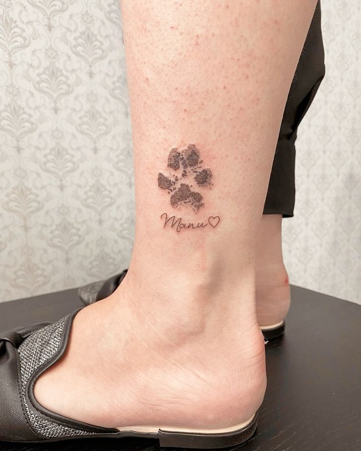 a woman's foot with a dog paw tattoo on her left ankle and the word mom written in cursive font