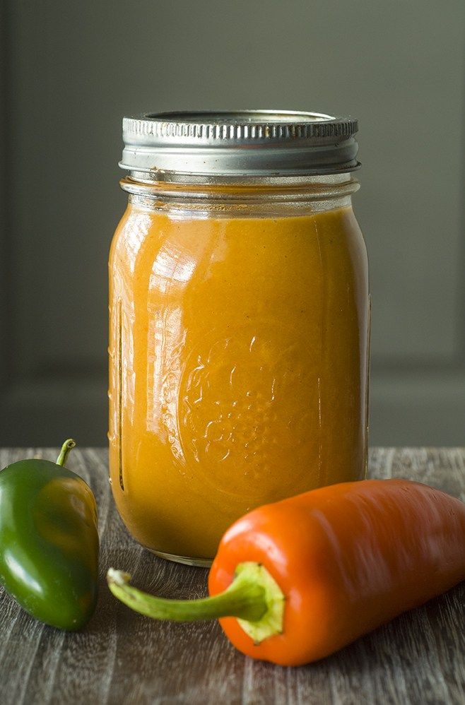 a glass jar filled with yellow liquid next to a green pepper