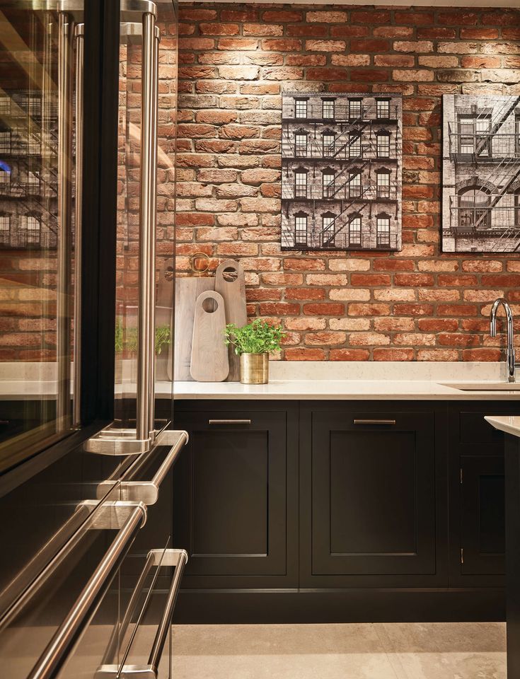 a brick wall in a kitchen with stainless steel sink and counter tops, along with black cabinets