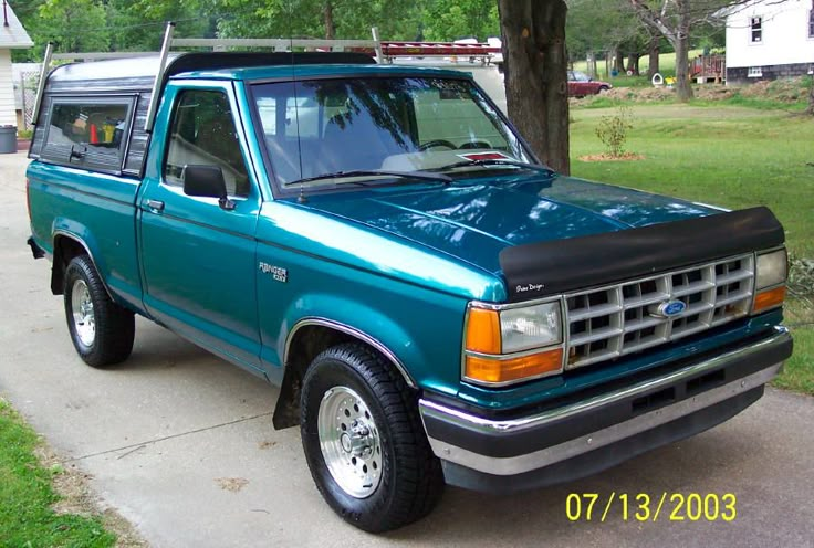 a blue pick up truck parked on the side of a road next to a tree