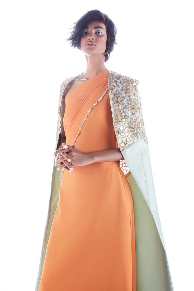 Orange double georgette saree gown with one shoulder neck, overlap pleated drapes, cut dana and bead tassel details.
Components: 1
Pattern: Hand Embroidered
Type Of Work: Cut Dana and Bead Work
Neckline: One Shoulder Neck
Sleeve Type: Sleeveless
Fabric: Double Georgette
Color: Orange
Other Details: 
Note: The cape worn by the model is not for sale
Occasion: Cocktail,Sangeet - Aza Fashions Saree Gowns, Draped Gown, Georgette Gown, Pleated Drapes, Drape Gowns, Gown For Women, Saree Gown, Drape Saree, Pleats Please