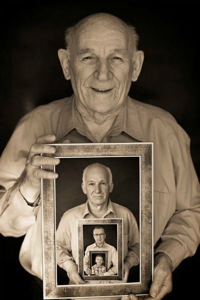 an old man holding up a framed photo with the image of himself in black and white