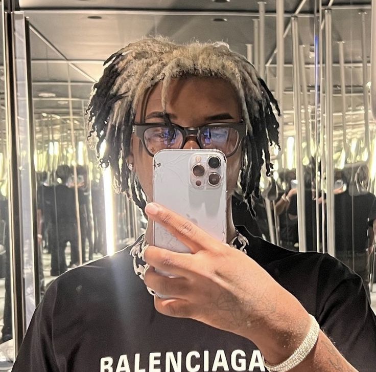 a man with dreadlocks taking a selfie in front of a mirrored wall