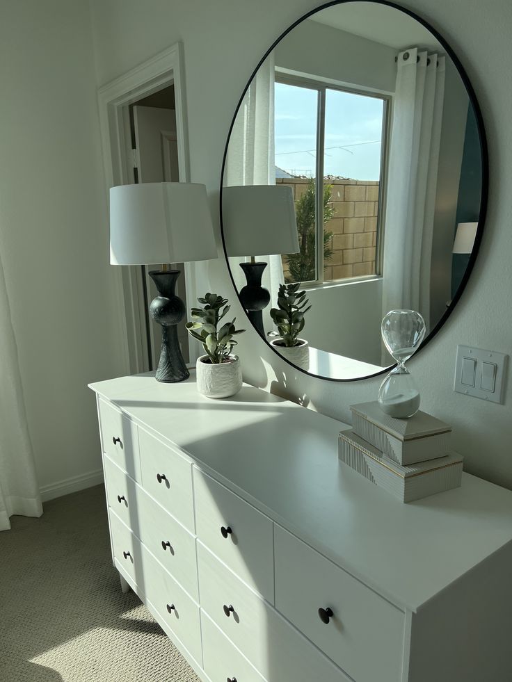 a white dresser topped with a mirror next to a window