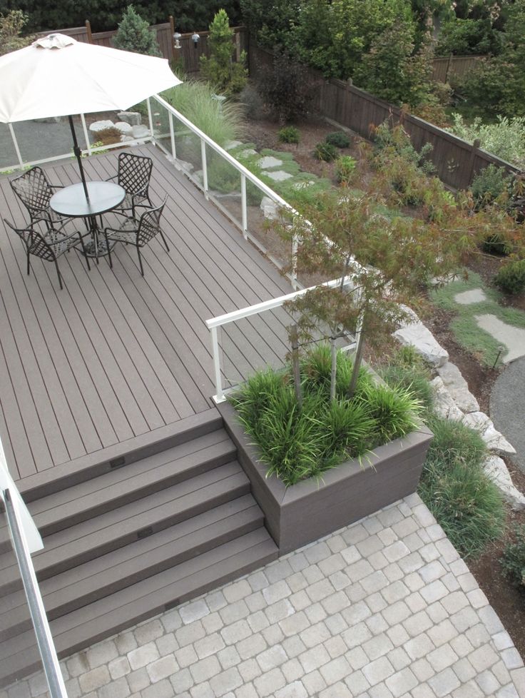 a patio with tables and chairs under an umbrella next to a stone path that leads up to the deck