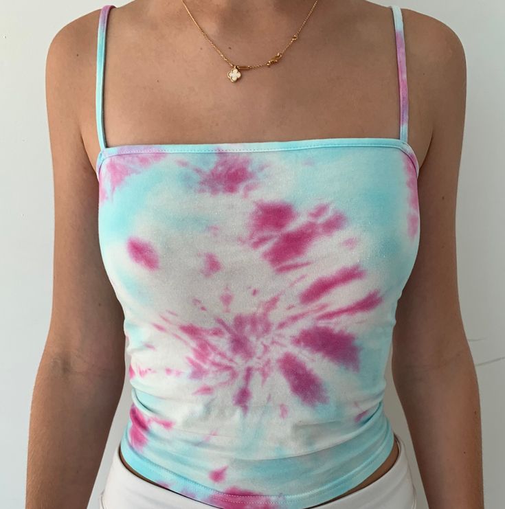 a woman wearing a tie dye shirt and white pants with a gold necklace on her neck