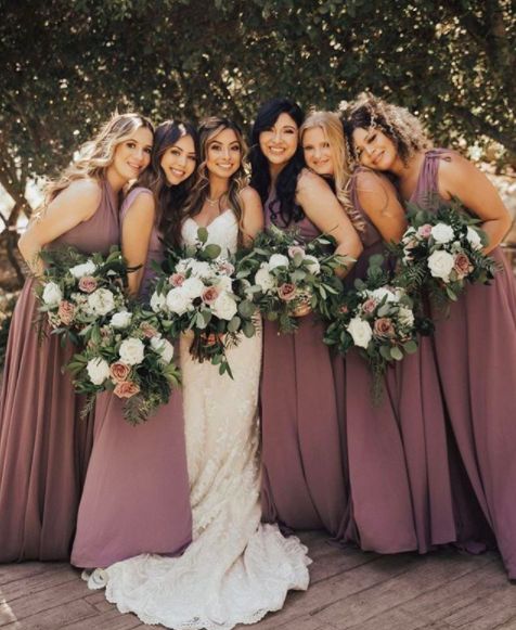 a group of women standing next to each other wearing dresses and holding bouquets in their hands