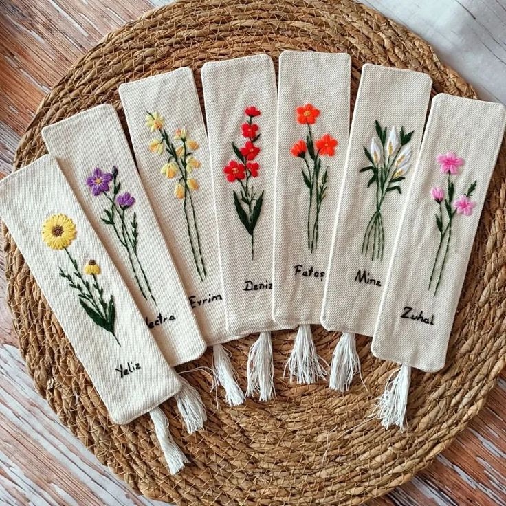 five embroidered napkins with flowers on them sitting on a wicker basket next to a wooden table