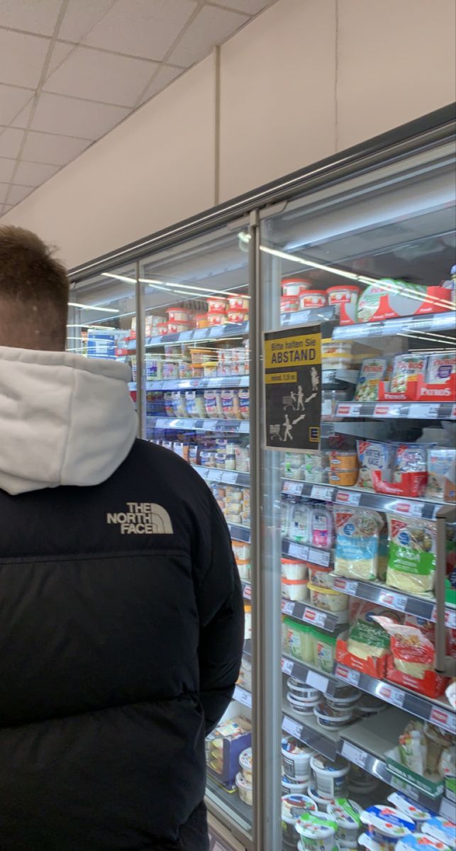 a man wearing a face mask standing in front of a display case filled with food