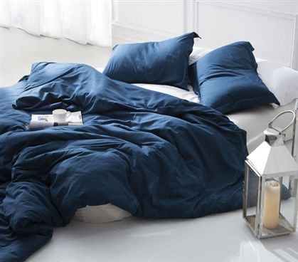 an unmade bed with blue sheets and pillows on the floor next to a lantern