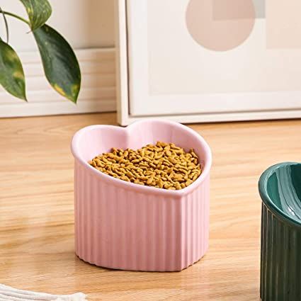 a pink heart shaped container filled with dog food next to a green trash can on a wooden floor