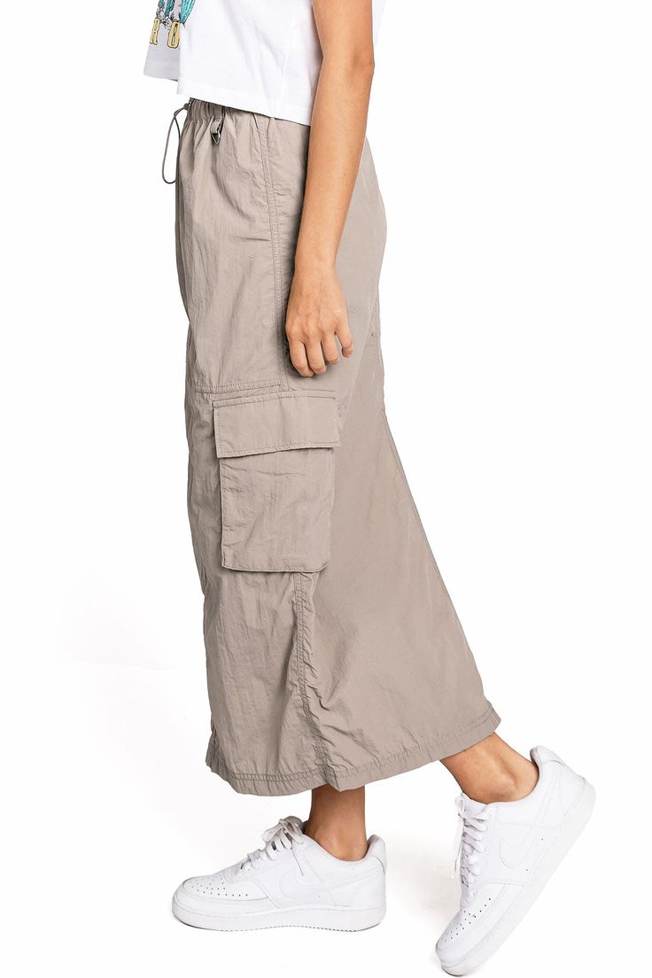 Chic, parachute skirt with an elastic waistband, a drawstring cinch tie and cargo pockets down the sides. Pair it with a graphic tee and sneakers for an effortless streetwear look. CARE | Machine Wash Cold CONTENTS | 100% Nylon MEASUREMENTS | 33"/85 cm Top to Bottom (Size Small) MODEL | 5'8 - wearing a size Small IMPORTED Casual Nylon Cargo Pants For Summer, Summer Casual Nylon Cargo Pants, Casual Cargo Skirt For Spring, Casual Summer Cargo Parachute Pants, Casual Nylon Bottoms With Elastic Waistband, Casual Summer Cargo Pants With Drawstring, Casual Cargo Skirt With Drawstring For Summer, Casual Summer Cargo Pants With Functional Drawstring, Casual Drawstring Cargo Skirt For Summer