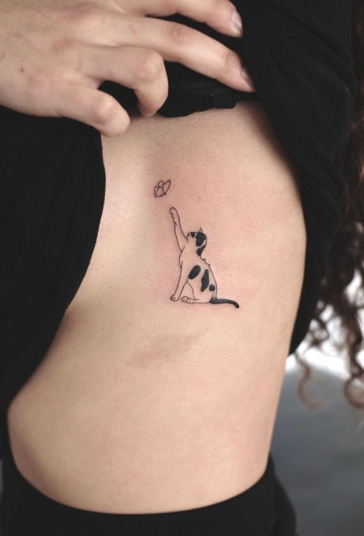 a woman's stomach with a small tattoo of a cat holding a ball in the air