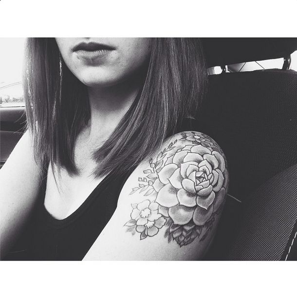 a woman sitting in a car with a flower tattoo on her arm and the rest of her arm behind her head