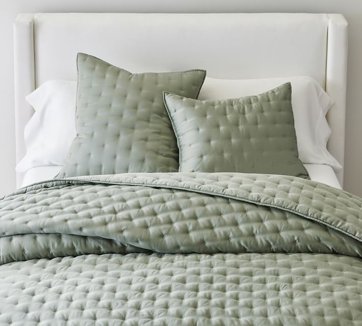 a bed with green comforter and pillows on it's headboard in a bedroom