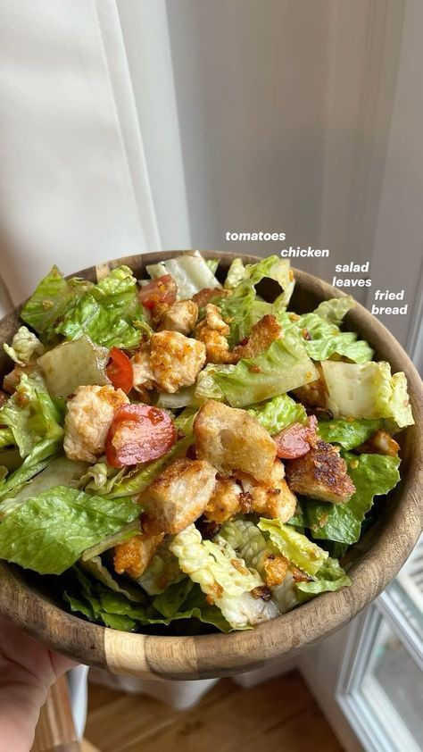 a wooden bowl filled with lettuce, bacon and tomato salad on top of a window sill