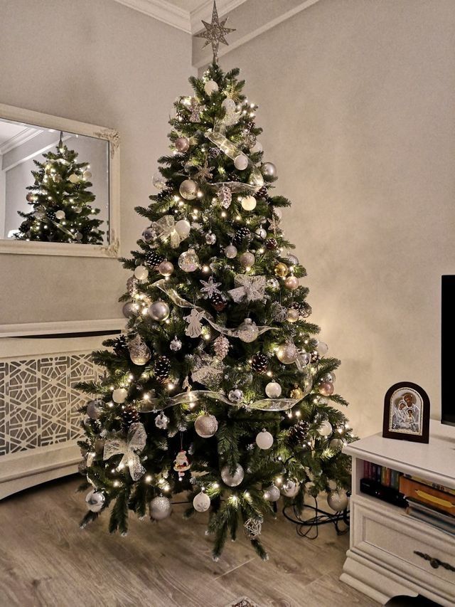 a decorated christmas tree in the corner of a living room with white and silver ornaments