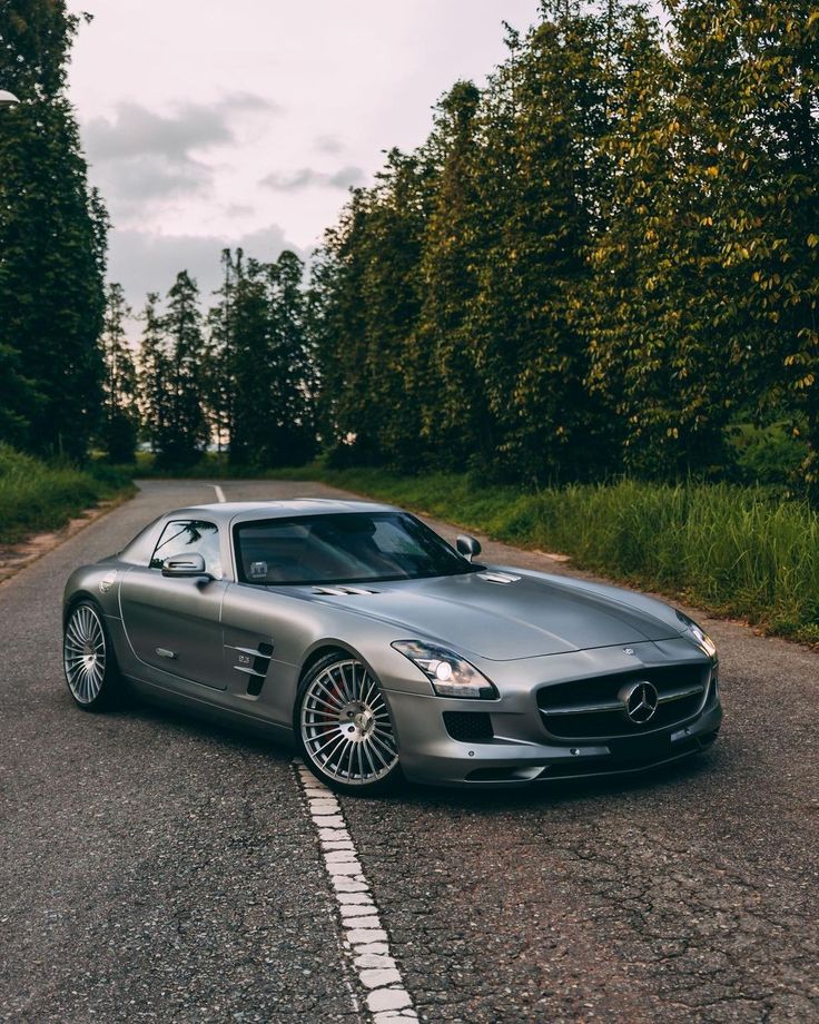 a silver sports car is parked on the side of the road in front of some trees