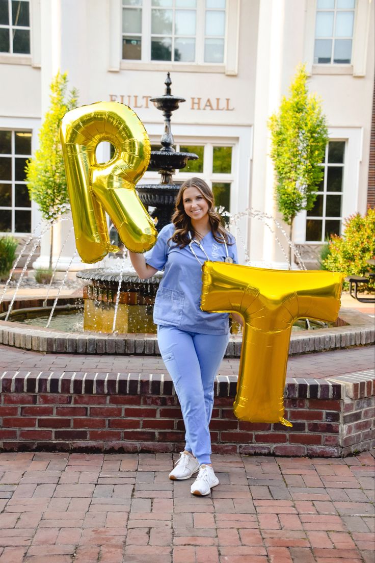 a woman in blue is holding up a large balloon shaped like the letter r and standing next to a fountain