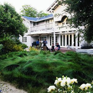 three people sitting on a bench in front of a large white house with tall grass