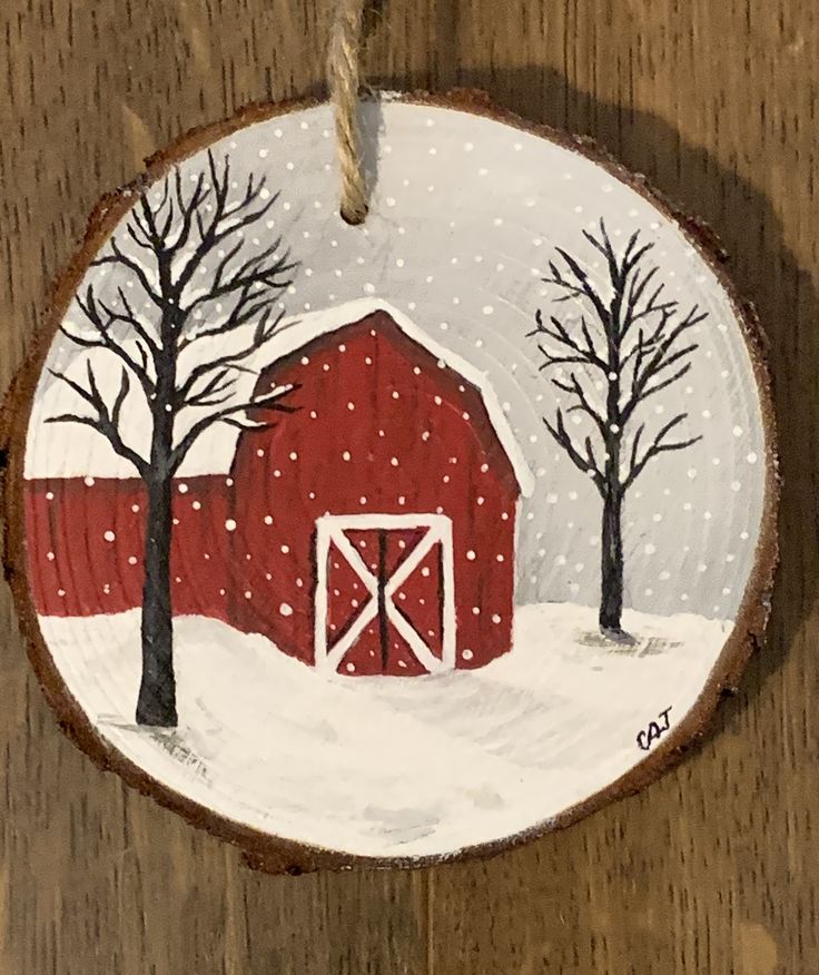 a christmas ornament with a red barn in the snow and trees painted on it