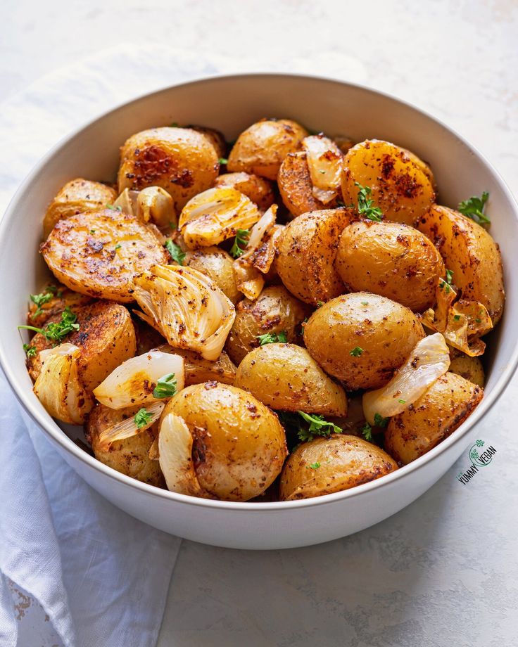 a white bowl filled with cooked potatoes on top of a table next to a napkin