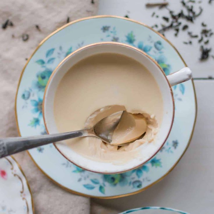 a spoon in a cup filled with liquid on top of saucer and plates next to it