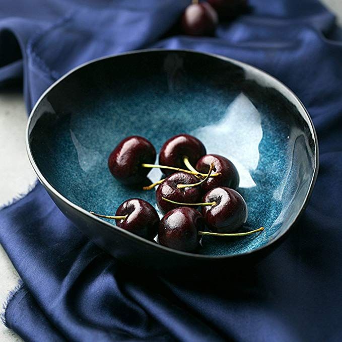 a blue bowl filled with cherries on top of a cloth covered table next to a napkin