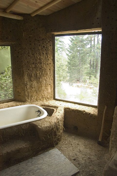 a bath tub sitting in the middle of a bathroom next to two large windows and a stone floor