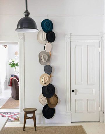 hats are hanging on the wall next to a chair and lamp in a room with white walls