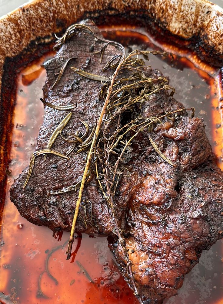 a piece of meat with some herbs on top of it in a bowl filled with liquid